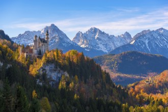 Neuschwanstein Castle stands against a picturesque backdrop of snow-capped mountains and autumn