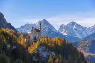 Neuschwanstein Castle rises majestically against snow-covered Alps in an autumnal landscape,