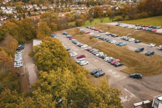 Large parking lot with various cars surrounded by slightly coloured autumn trees, Calw District