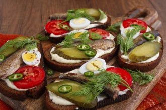 Sandwiches on rye bread with sprats, quail eggs, fresh tomatoes and pickled cucumber, on a wooden