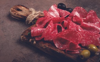 Sliced salami sausage, on a wooden chopping board, decorated with olives and herbs, close-up, no
