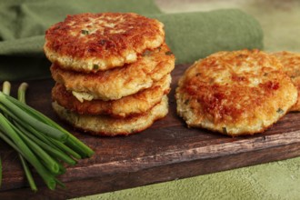 Crispy potato pancakes Latkes, stacked on a wooden board next to fresh green onions, natural light,