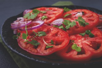 Freshly sliced tomatoes and red onions, garnished with herbs, on a black plate, summer salad, no