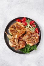 Baked quail, served on a plate with crispy lettuce leaves, fresh tomatoes and herbs, on a dark