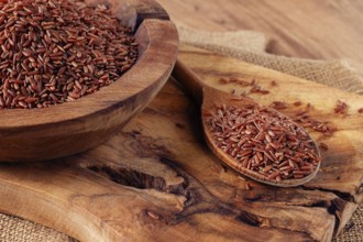 Natural, red rice, in a wooden bowl and spoon on a wooden surface in rustic style, top view