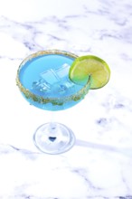 Bright blue cocktail with a slice of lime on a marble surface