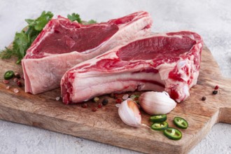 Fresh pieces of beef on the bone, on a wooden cutting board, with herbs and spices, ready for