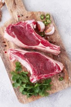 Fresh pieces of beef on the bone, on a wooden cutting board, with herbs and spices, ready for