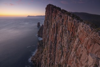 Long exposure at sunrise shows the glowing dawn over the huge rocks of Cape Hauy. Waves hit the