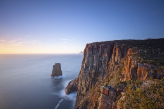 Long exposure at sunrise shows glowing dawn over the dramatic cliffs of Cape Hauy. View towards