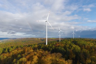 Wind turbines rise above an autumnal forest with a rainbow in the background, near Schorndorf,