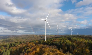 Wind turbines stand over an autumnal forest with a rainbow in the sky, near Schorndorf, Remstal,