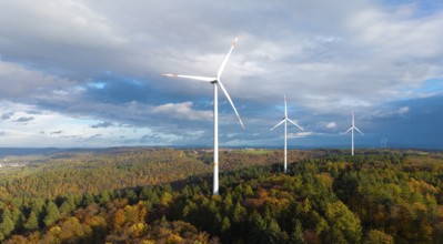 Three wind turbines above a colorful autumn forest against a cloudy sky, near Schorndorf, Remstal,