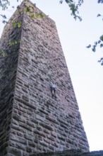 A climber climbs the stone wall of a tower, accentuated by clear air and natural surroundings,
