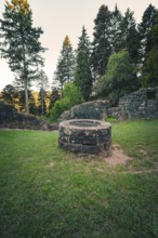 A historic well surrounded by ruins, surrounded by forest and illuminated by soft evening light,