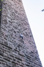 A climber climbs a massive stone tower surrounded by trees and blue sky, Mandelberg Castle Ruins,