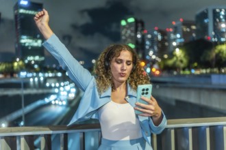 Young woman with curly hair wearing headphones and an elegant blue outfit, expressing joy and