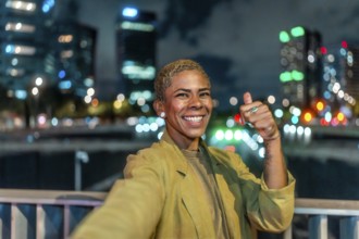 Happy young woman with short blonde hair and a radiant smile is taking a selfie gesture and showing