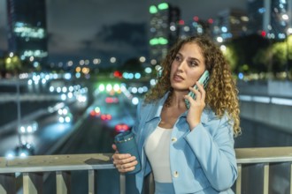 Professional businesswoman standing on a city bridge at night, having an important phone call with