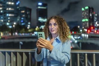 Young woman with curly hair looking surprised while holding a mobile phone, discovering new content