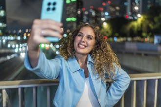 Young woman with curly hair smiling happily while capturing a selfie on her mobile phone, standing