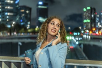Young woman with curly hair talking on phone with a worried expression while holding a reusable