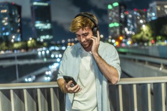 Young man smiling and listening to music through wireless headphones, holding a smartphone while