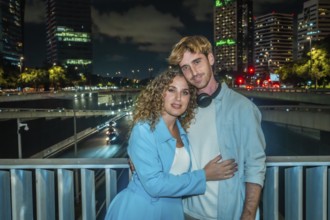 Young couple embracing on an urban bridge at night, city skyline and streaking highway lights