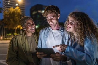 Cheerful diverse friends laughing and sharing content on a tablet while standing together on a city