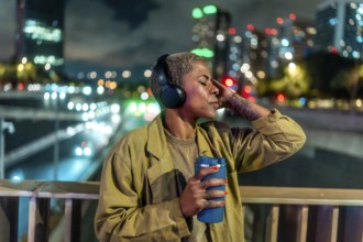 Woman with short hair, wearing headphones and holding a travel mug, relaxing with closed eyes on an