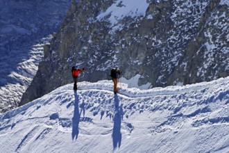 Two mountaineers run across a snow-covered mountain ridge, Aiguille du Midi, Chamonix-Mont-Blanc,