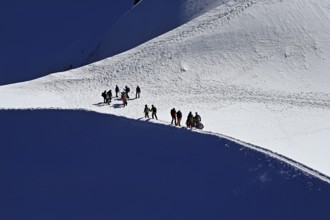 A group of mountaineers runs across a snow-covered mountain ridge, Aiguille du Midi,