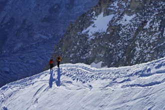 Two ascended mountaineers run across a snow-covered mountain ridge, Aiguille du Midi,