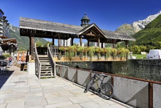 Old wooden bridge decorated with flowers that crosses the glacial river Arve, Chamonix-Mont-Blanc,