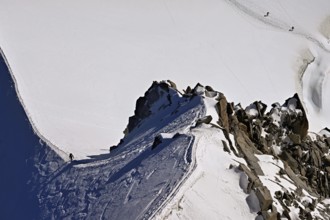 A mountaineer climbs over a snow-covered mountain ridge, Aiguille du Midi, Chamonix-Mont-Blanc,
