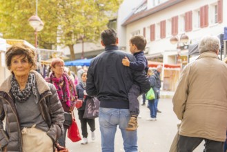 Visitors in autumn clothes stroll while a man carries a child, Streuobstmarkt, Sindelfingen,