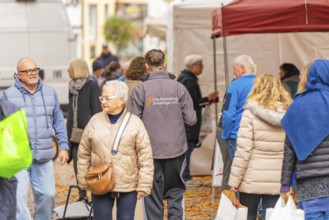 People wearing autumn clothes visit a market while the ground is covered with leaves,