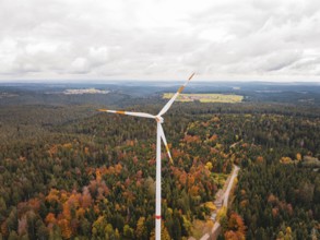 Large wind turbine over colorful autumn forest with nearby fields, Simmersfeld wind farm, Germany