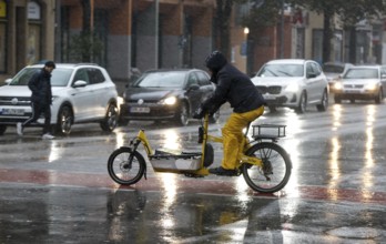 A man rides a cargo bike across a rained road in heavy rain, Berlin, 30.10.2025, Berlin, Berlin,