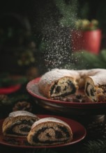 Icing sugar falls on poppy seed cake on red plate surrounded by Christmas decorations