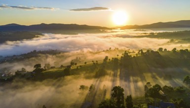 Sunrise over a fog covered village in a rural landscape, golden morning light, serene autumn