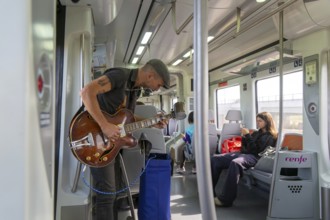 Musician busker playing guitar onboard train of Rodalia de Barcelona suburban rail network,