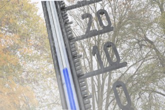 (photo montage) Thermometer in front of autumn-colored deciduous tree shows cool temperatures