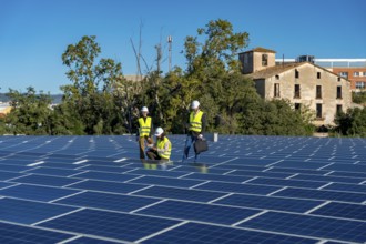 Three engineers wearing safety helmets and vests performing an inspection of a large rooftop solar