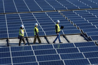 Three engineers walking on a rooftop solar power station, checking and inspecting the large array
