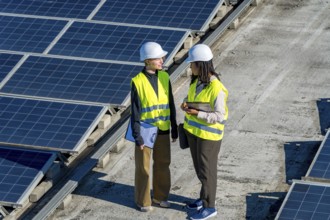 Two diverse female engineers in hard hats and vests discussing an ongoing project while standing on