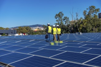 Team of engineers is inspecting an array of solar panels on a rooftop power plant, working on a