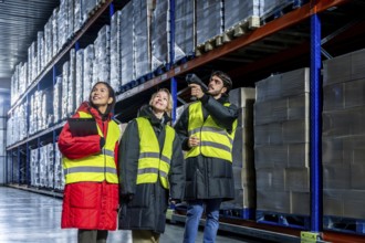 Diverse warehouse team in safety vests and warm protective gear scanning and checking inventory on