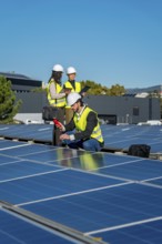 Engineers in hard hats and safety vests are examining solar panels on a rooftop, checking