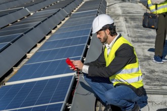 Engineer in hard hat and safety vest inspecting rooftop solar panels with a multimeter, monitoring